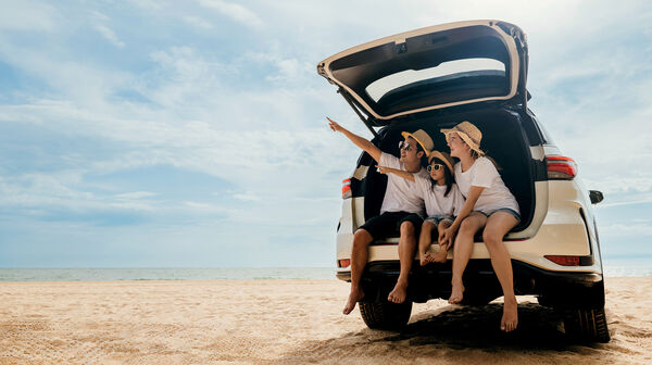 Eine Mutter mit zwei Kindern sitzt im Kofferraum eines Autos am Strand