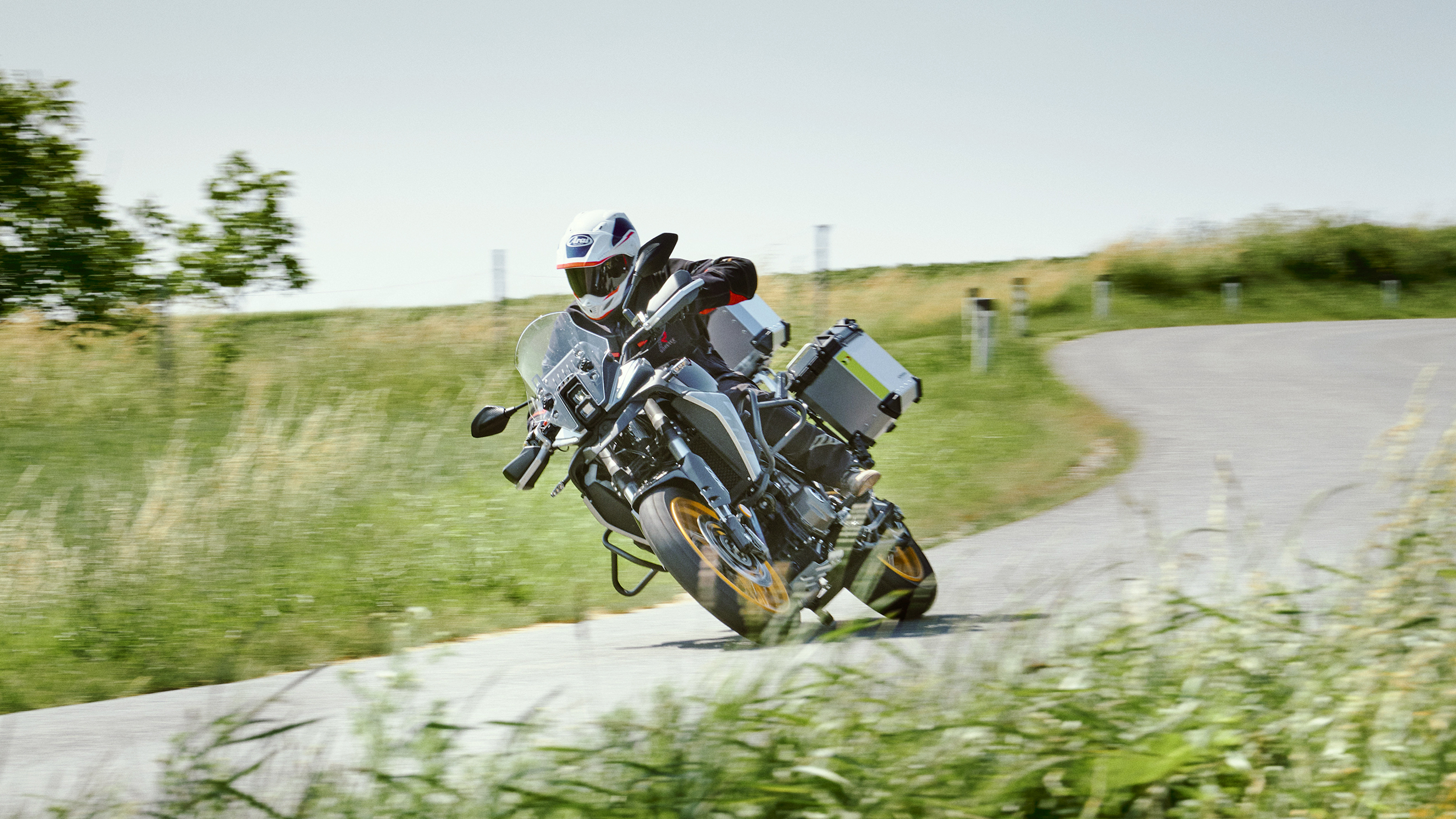 Die Reisenduro fährt in Schräglage eine Rechtskurve auf einer Landstraße entlang.