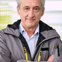 Das Bild ist ein Portrait von Steffan Kerbl, der frontal in die Kamera schaut, eine graue Jacke mit gelber ÖAMTC-Aufschrift trägt und die Arme verschränkt.