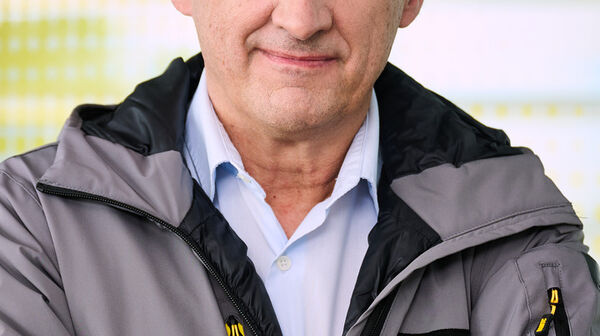 Das Bild ist ein Portrait von Steffan Kerbl, der frontal in die Kamera schaut, eine graue Jacke mit gelber ÖAMTC-Aufschrift trägt und die Arme verschränkt.