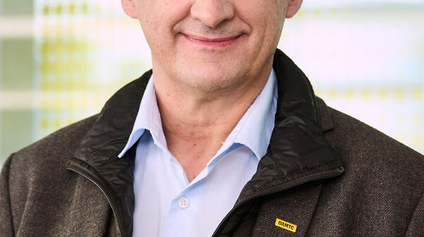 Porträt eines Mannes mit grauem Haar, blauen Hemd und grauer Jacke vor einer Glaswand