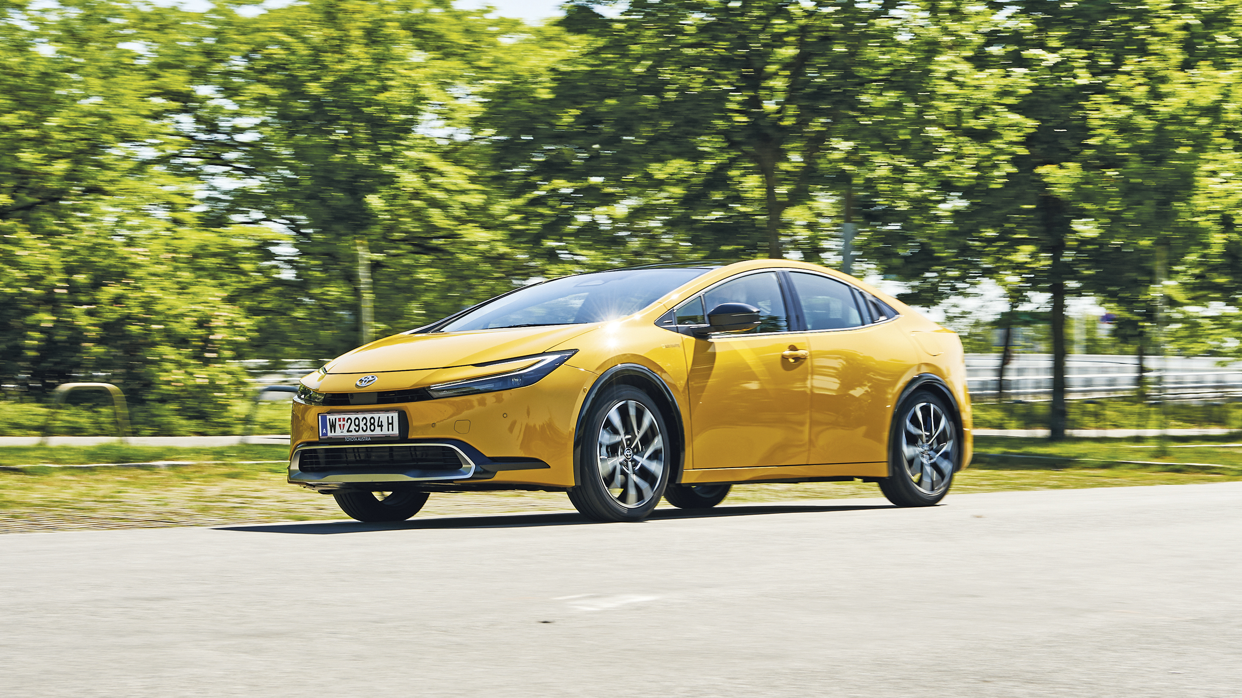 Fahrender Toyota Prius in grüner Landschaft.