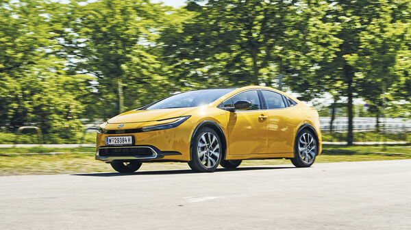 Fahrender Toyota Prius in grüner Landschaft.