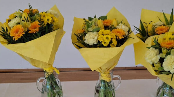 Das Foto zeigt fünf Blumensträuße mit gelbem Geschenkpapier umwickelt. Die Blumen selbst sind ebenfalls gelb und orange.