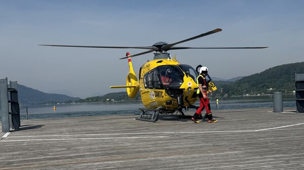 Christophorus-Hubschrauber steht auf einem Steg am See. Vor dem Hubschrauber geht ein Crew-Mitglied.