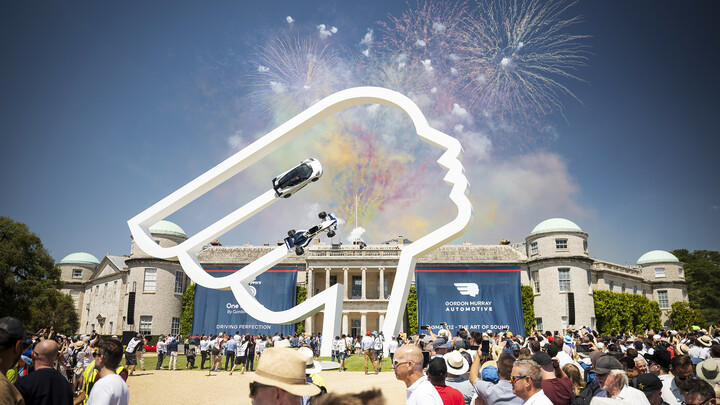 Feuerwerk über einem Schloss. Davor steht ein Kunstwerk mit zwei Fahrzeugen.