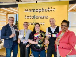 Veranstaltung der Queer Angels (v.l.n.r.: ÖAMTC-Direktor Ernst Kloboucnik, Edina, Ursula, Jürgen und ÖAMTC-Diversitätsmanagerin Pamela Rath) Es stehen fünf Personen vor einer gelben Wand. Die Personen halten jeweils Regenbogenfahne und andere Accessoires in Regenbogenfarben.