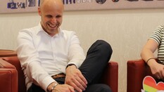 Jürgen spricht von seinen Erfahrungen beim ÖAMTC. Das Bild zeigt einen Mann, der auf einem roten Sessel sitzt. Er trägt eine dunkle Hose und ein weißes Hemd und lacht.