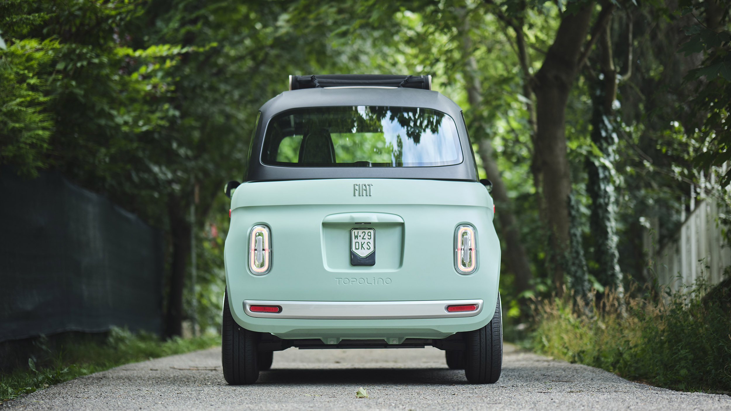 Ein türkises Microcar steht auf einer Straße, die von Bäumen umgeben ist.
