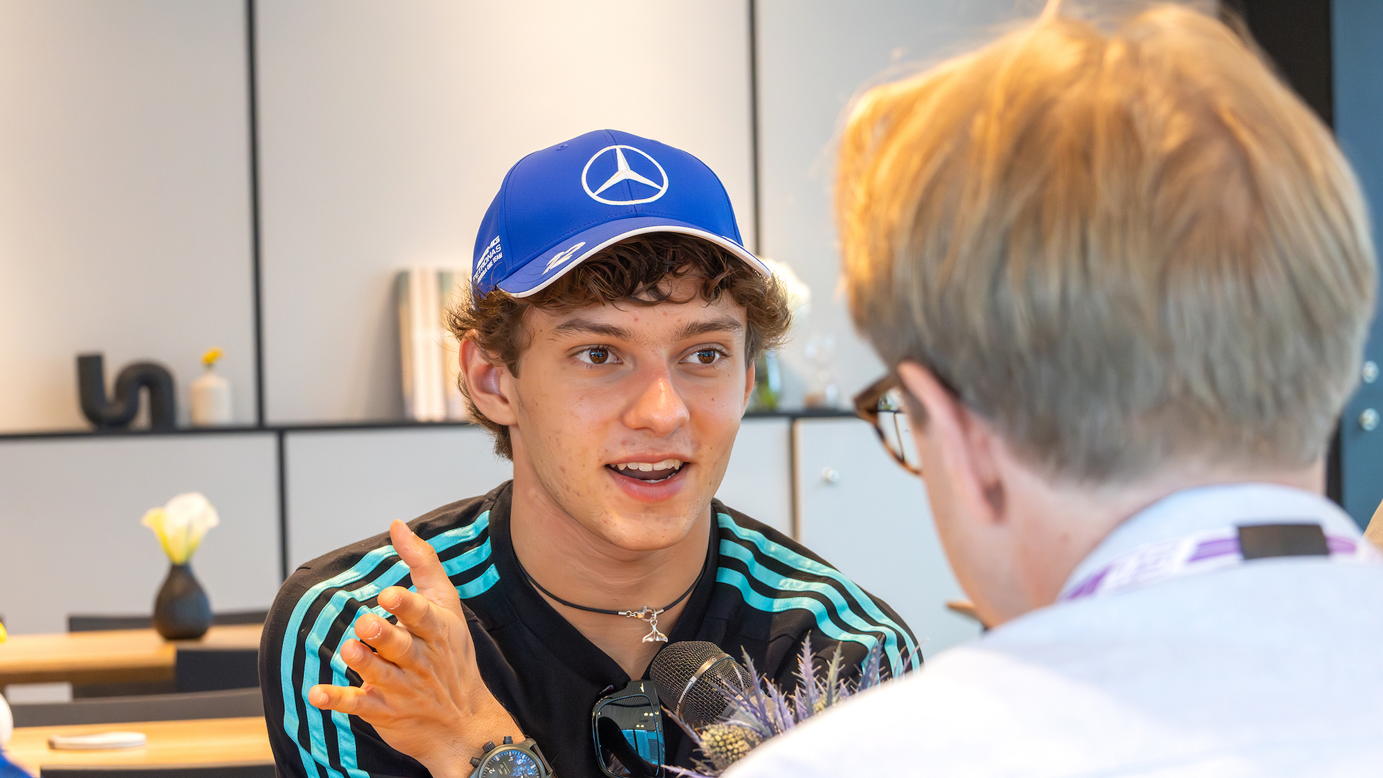 Der Formel-1-Fahrer Kimi Antonelli spricht mit einem Journalisten und trägt dabei eine blaue Mercedes-Kappe.