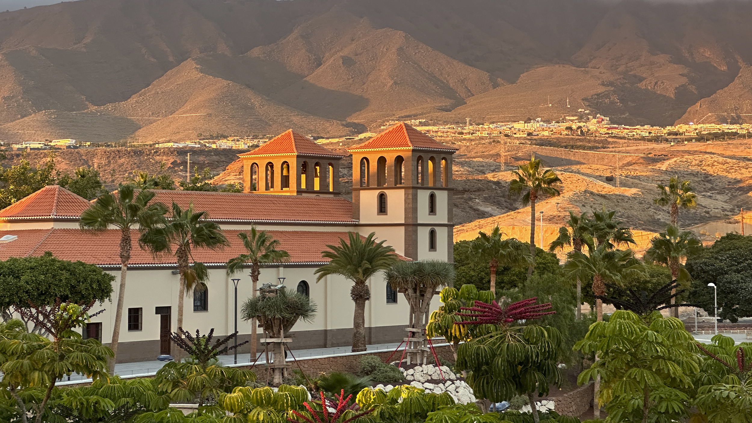Eine Kirche mit zwei Türmen umgeben von Palmen in einer wüstenähnlichen Landschaft.