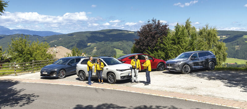 vier elektroautos stehend auf parkplatz dazwischen vier personen