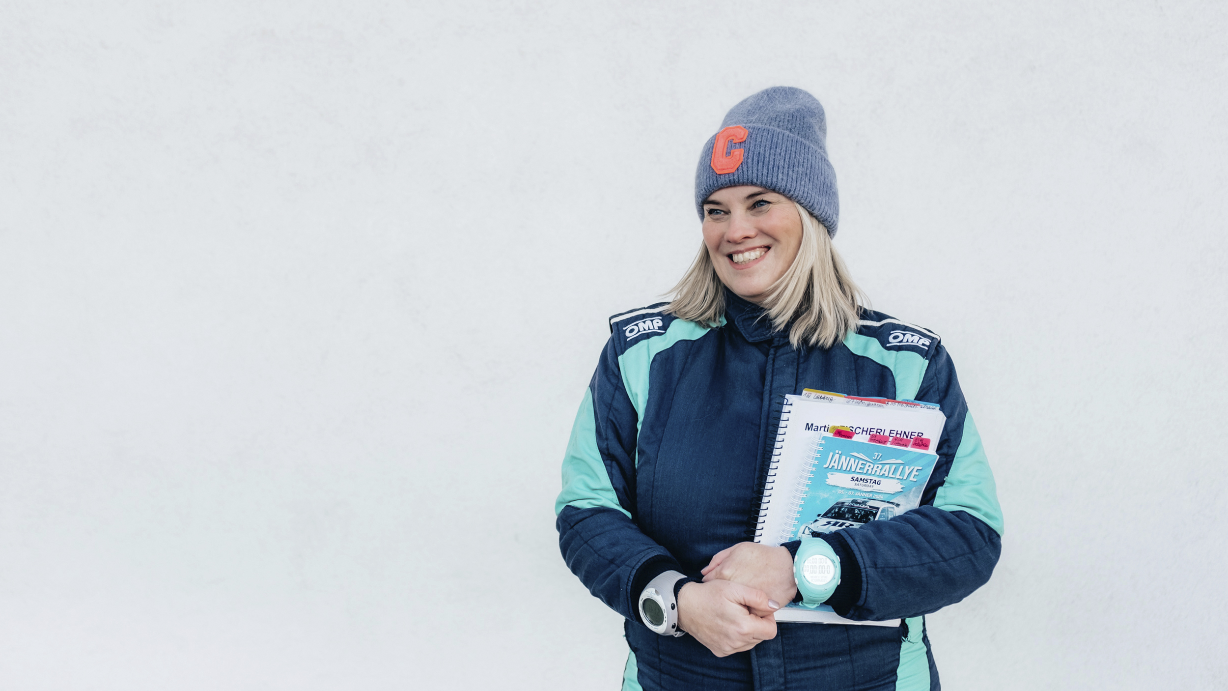 Catharina Schmidt, Rallye-Co-Pilotin und ÖAMTC-Mitarbeitetin steht im Renndress vor hellgrauem Hintergrund und hält ihre Rennnotizen in der Hand.