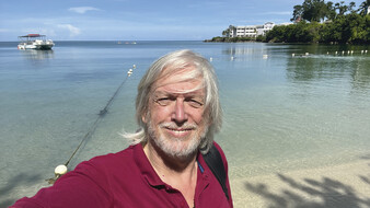 Redakteur Peter lacht in die Kamera für das Selfie, hinter ihm das Meer.