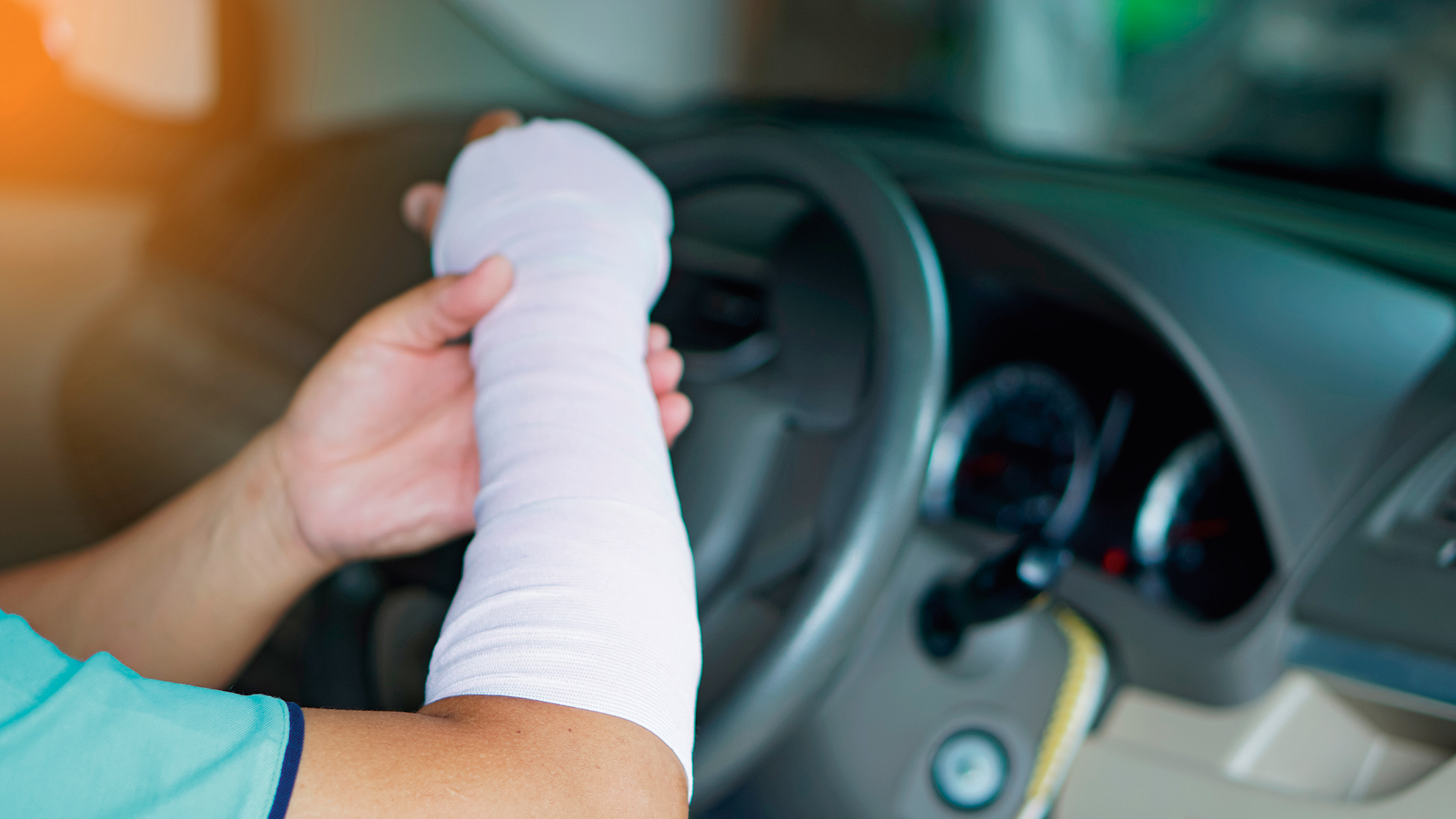 Ein verletzter Mann mit einem Verband an Hand und Arm fährt ein Auto, was zu einem Unfall führen könnte, weil es unbequem ist, wie mit einer normalen Hand zu fahren.
