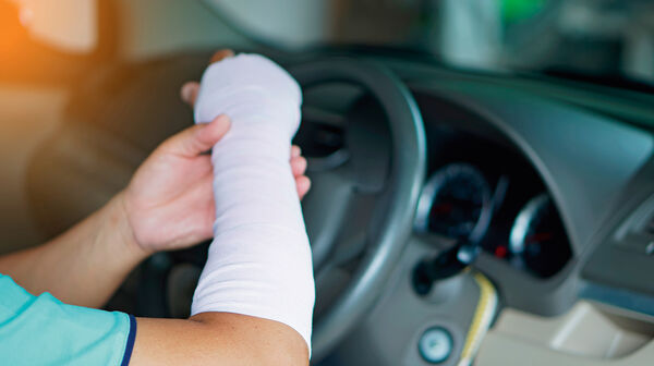 Ein verletzter Mann mit einem Verband an Hand und Arm fährt ein Auto, was zu einem Unfall führen könnte, weil es unbequem ist, wie mit einer normalen Hand zu fahren.