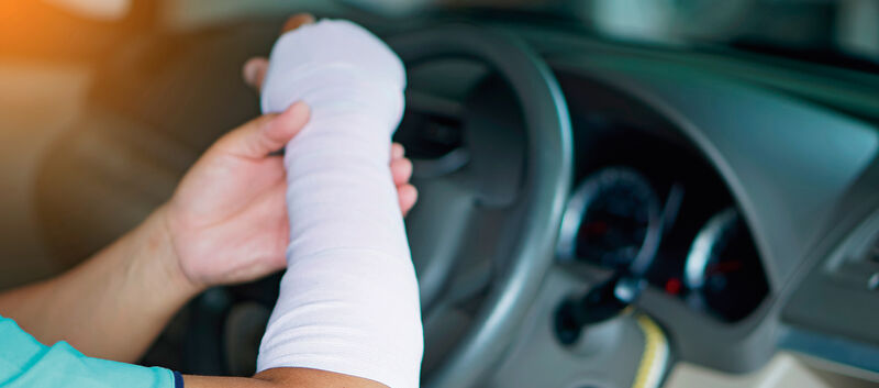 Ein verletzter Mann mit einem Verband an Hand und Arm fährt ein Auto, was zu einem Unfall führen könnte, weil es unbequem ist, wie mit einer normalen Hand zu fahren.