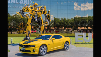 Ein gelbes Auto steht vor einer überlebensgroßen Transformers-Figur