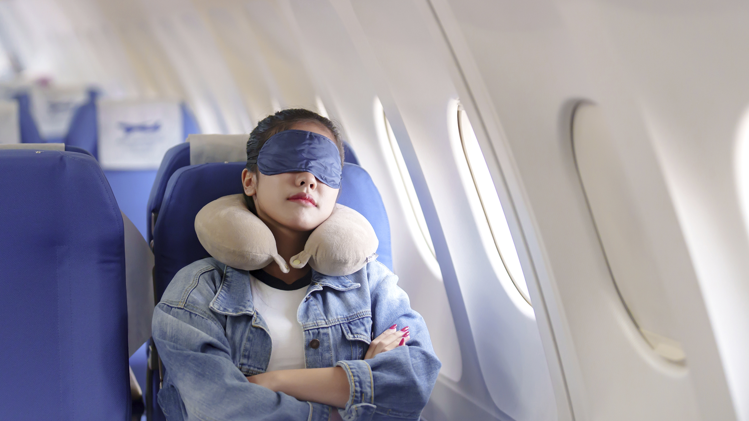 Frau schläft mit Schlafmaske in Flugzeug.