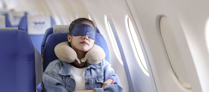 Frau schläft mit Schlafmaske in Flugzeug.