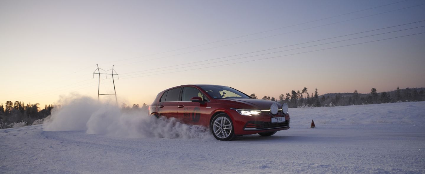 Rotes Auto fährt auf Schneefahrbahn bei Sonnenaufgang