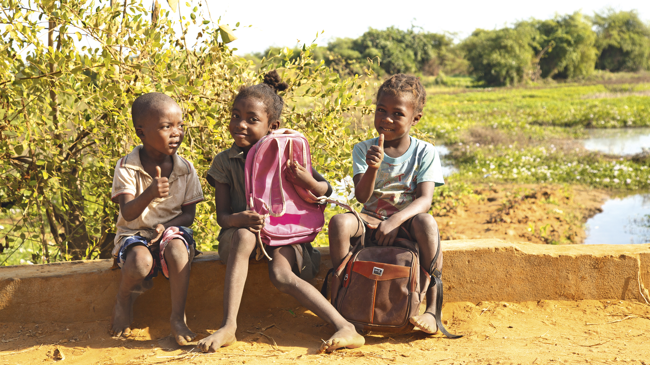 Drei Kinder sitzen mit ihrem Rucksack.
