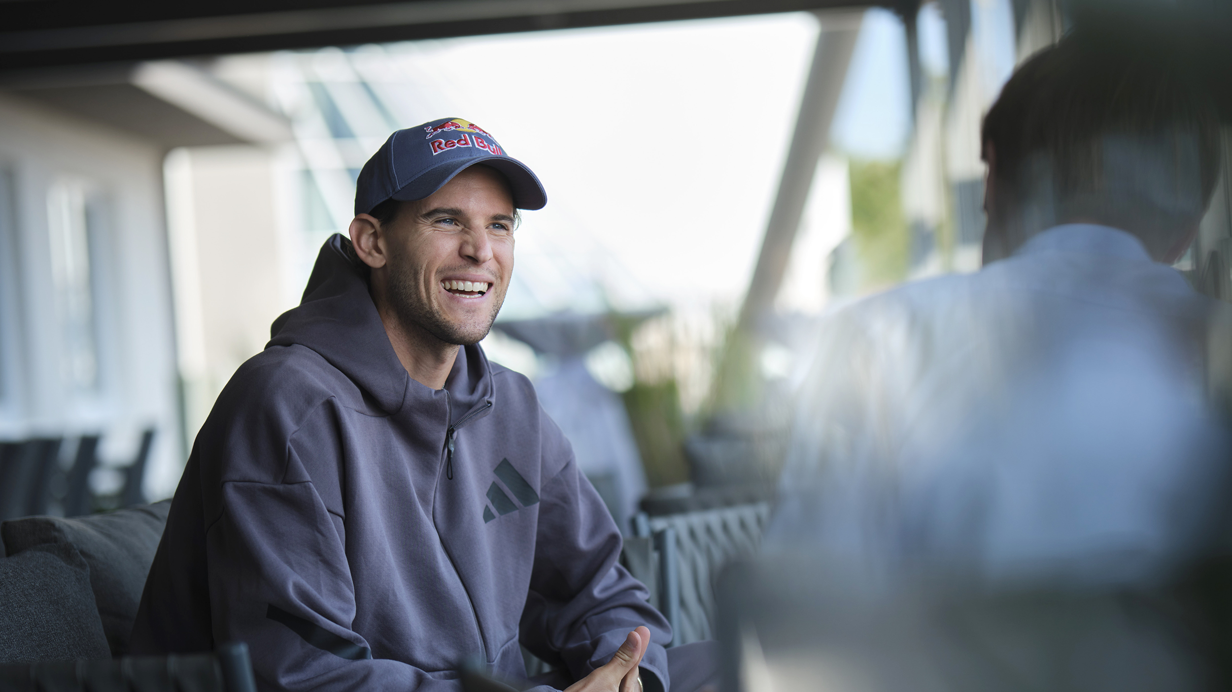 Der Ex-Tennisspieler Dominic Thiem mit Kappe und grauem Kapuzenpullover im Gespräch mit einem Journalisten.