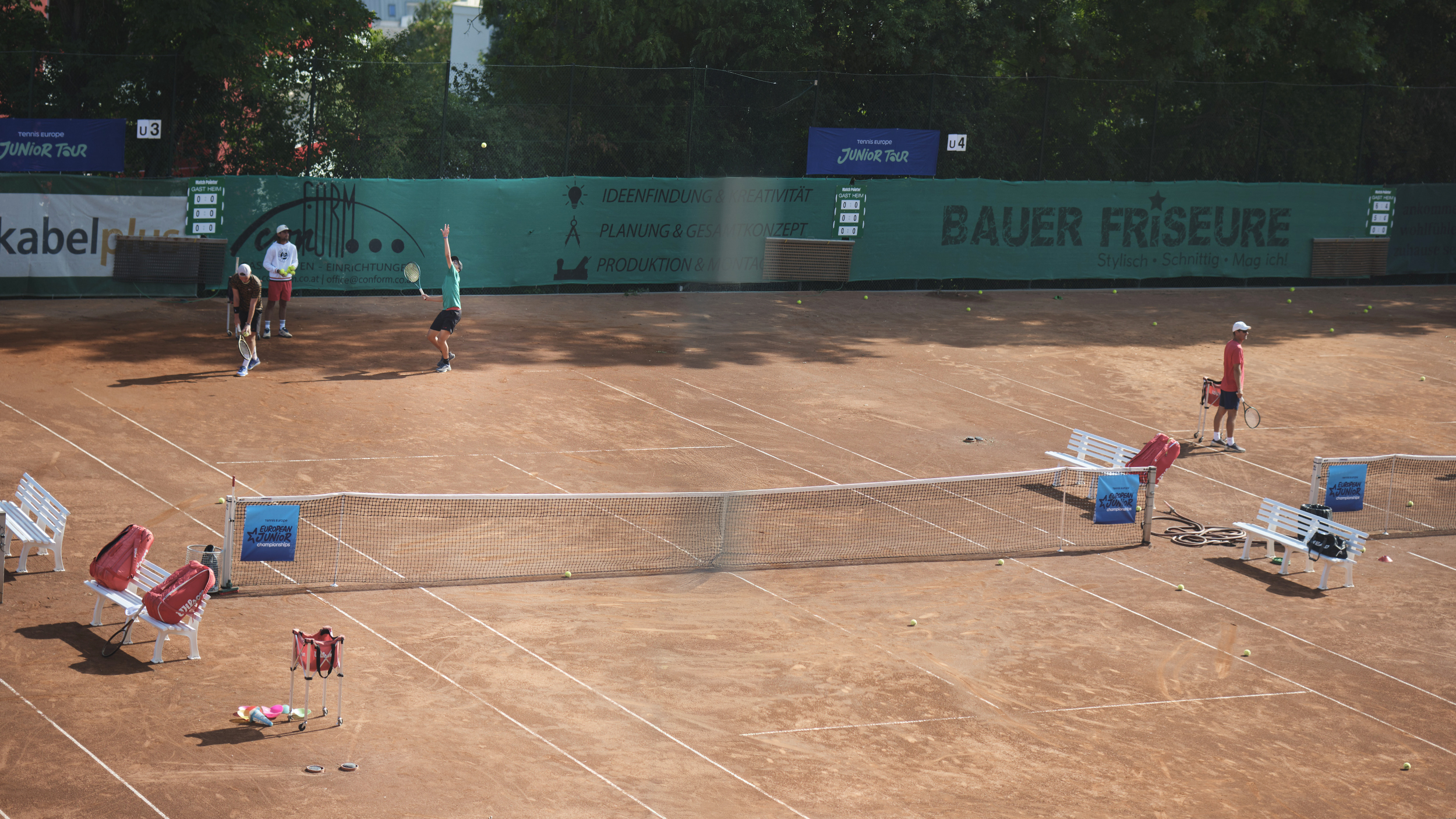 Auf einem Tennis-Sandplatz schlägt ein Spieler in grünem T-Shirt auf,