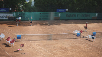Auf einem Tennis-Sandplatz schlägt ein Spieler in grünem T-Shirt auf,