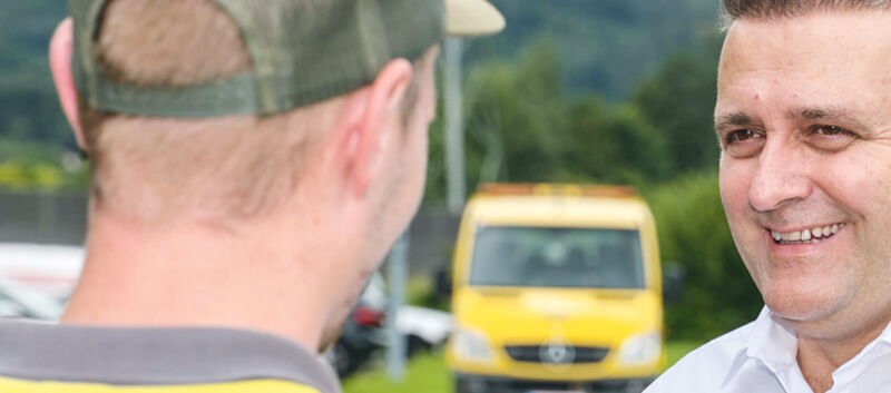 Auf dem Bild sieht man einen jungen Mann von Hinten im Gespräch mit einem ihm zugewandten Mann im weißen Hemd.