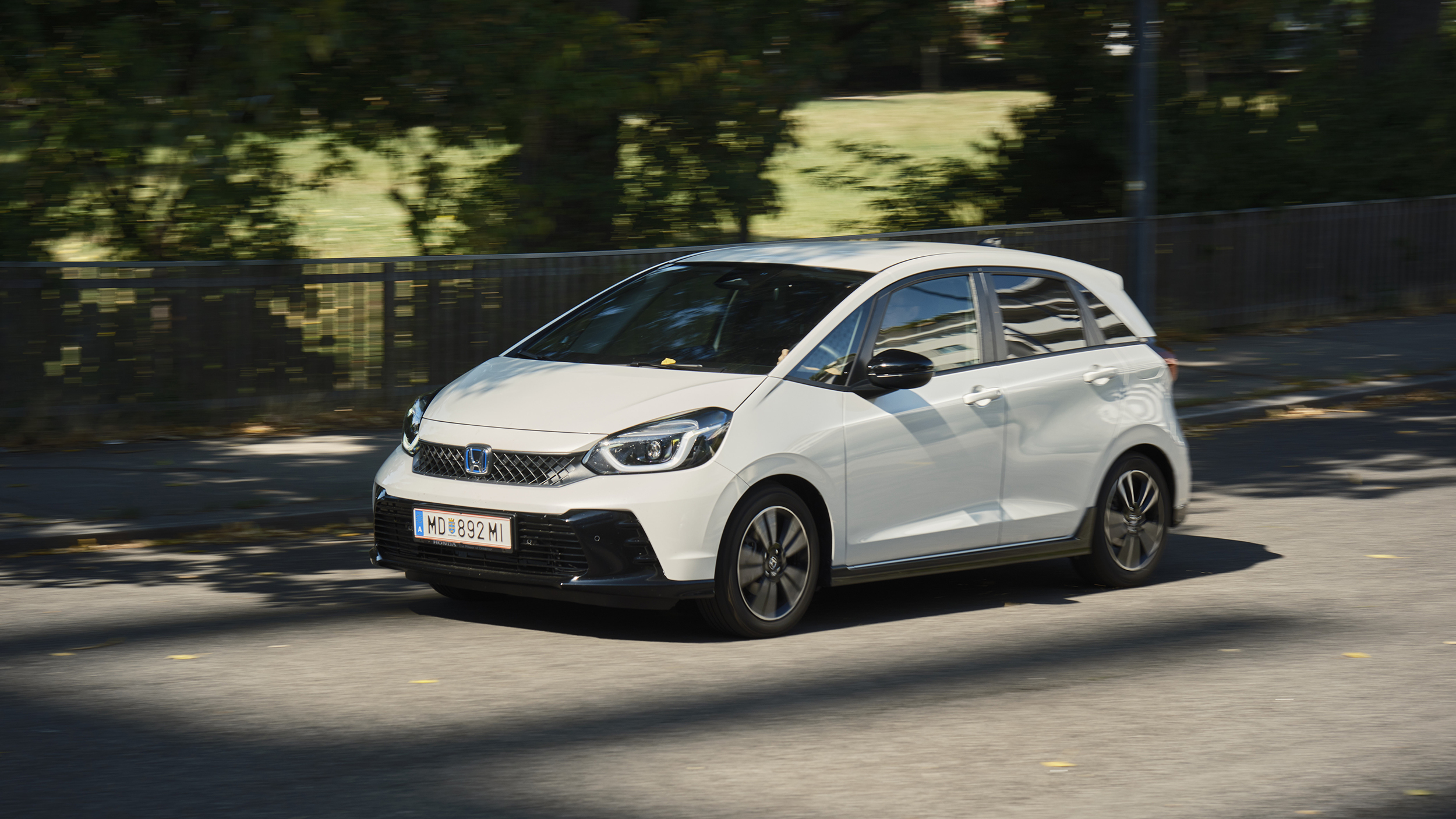 Ein weißer Honda Jazz fährt an einem Park vorbei