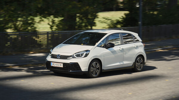 Ein weißer Honda Jazz fährt an einem Park vorbei