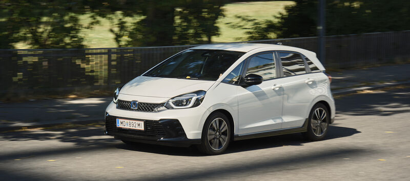 Ein weißer Honda Jazz fährt an einem Park vorbei