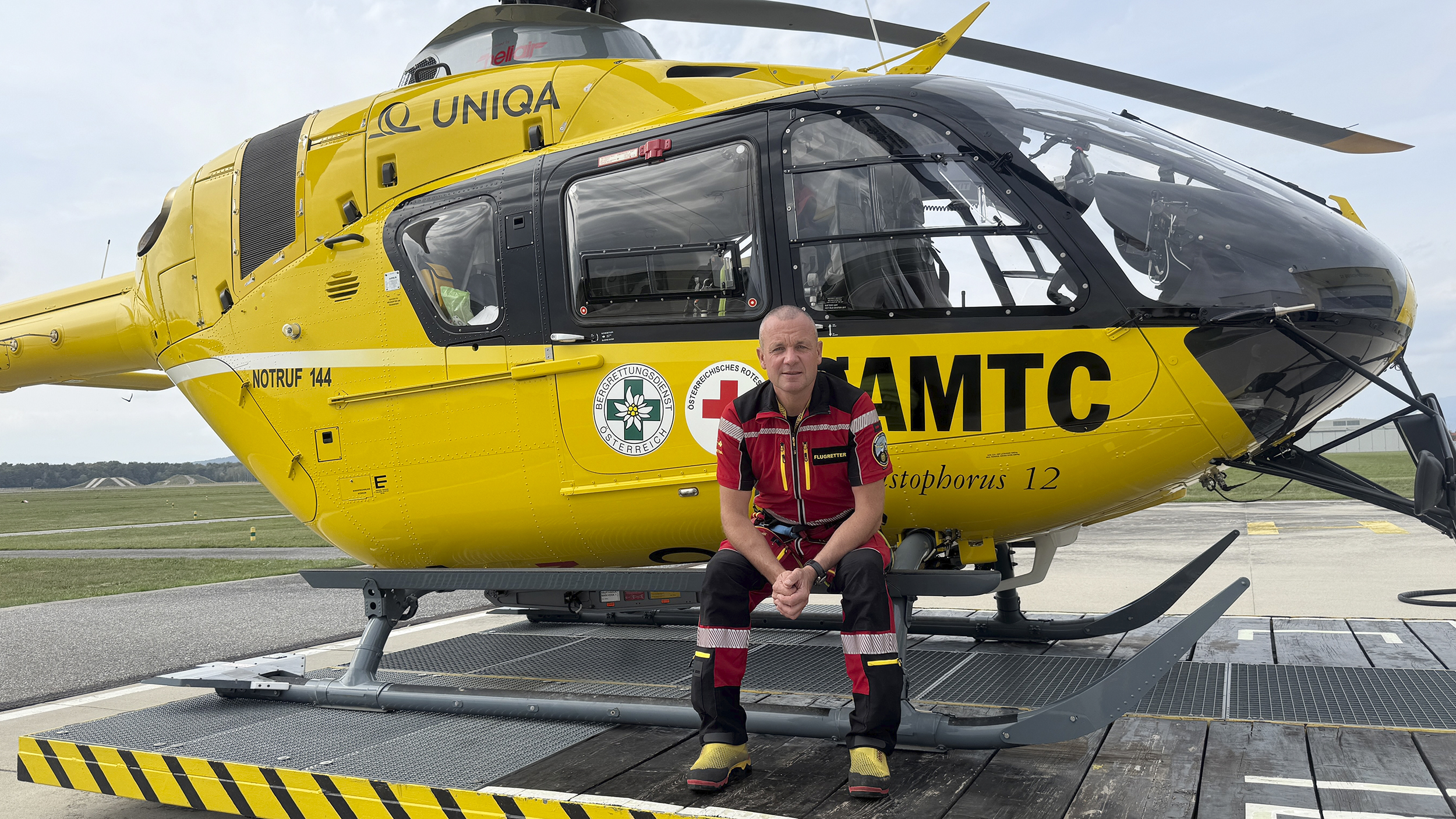 Flugretter Markus Amon sitzt in seiner Uniform vor einem Christophorus Helikopter.