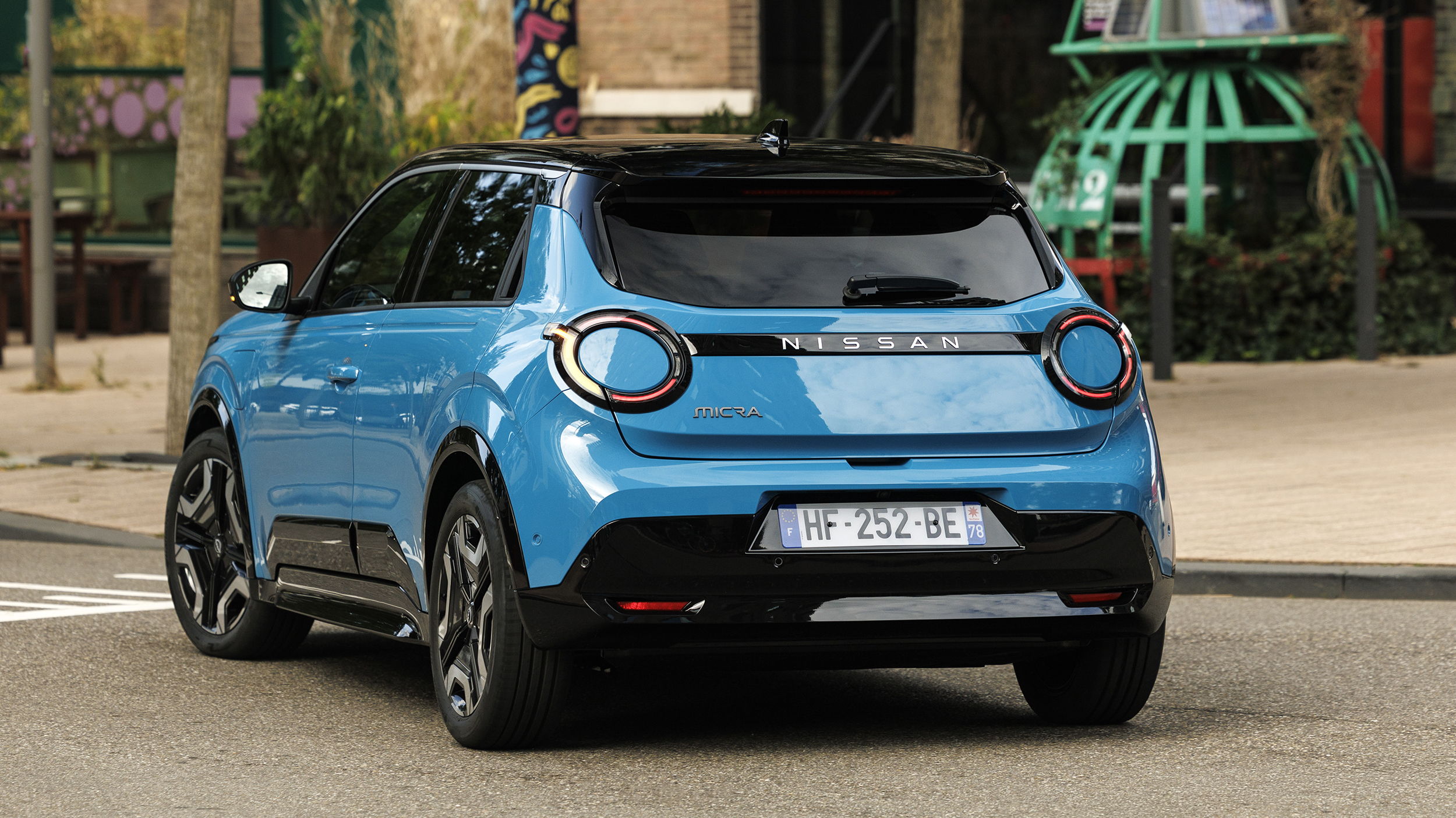 Heck eines blauen Nissan Micra, der vor einem Backsteingebäude steht. 
