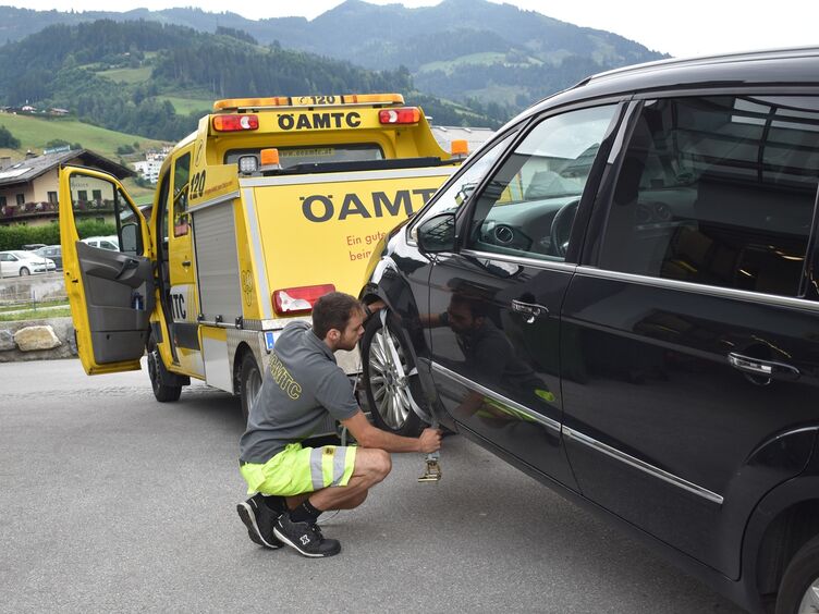 Das Bild zeigt Pannenfahrer Daivd, wie er neben einem schwarzen Auto kniet und einen Gurt festmacht, um dieses Auto mit dem Pannenfahrzeug abzuschleppen.