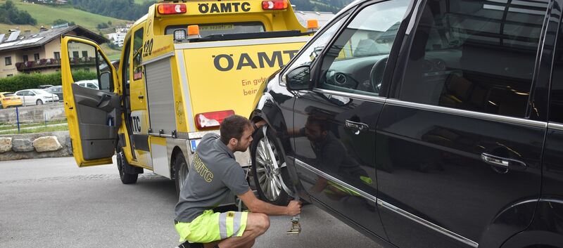 Das Bild zeigt Pannenfahrer Daivd, wie er neben einem schwarzen Auto kniet und einen Gurt festmacht, um dieses Auto mit dem Pannenfahrzeug abzuschleppen.