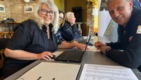 Auf dem Bild sieht man eine Frau und einen Mann an einem Tisch sitzen. Beide lachen in die Kamera. Auf dem Tisch liegen zwei geöffnete Ordner.
