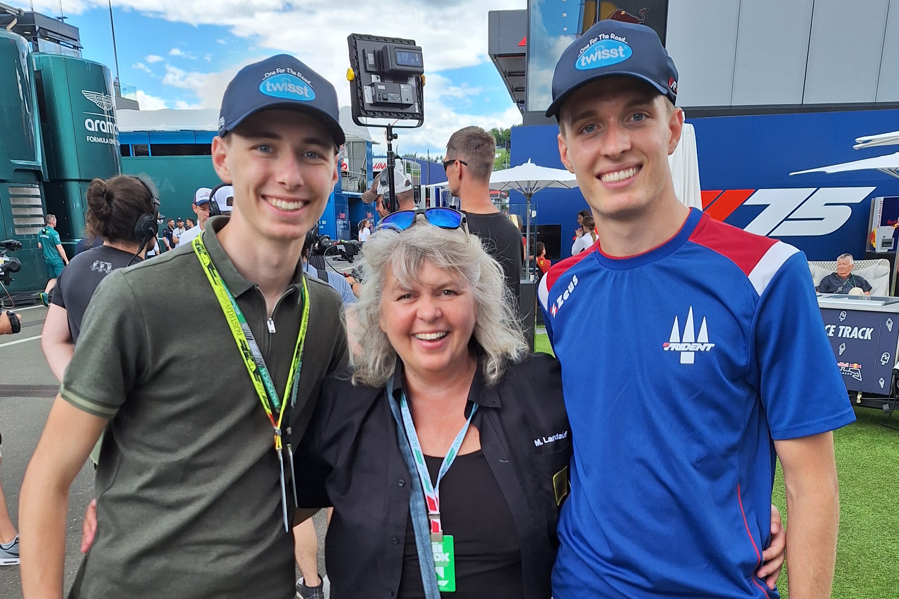 Auf dem Bild sieht man eine Frau flankiert von zwei Jugendlichen neben einer Rennstrecke.