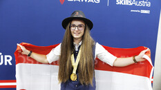 Pannenfahrerin Leonie Tieber mit Steirerhut und Medaille nach ihrem Sieg bei den Euroskills 2025. Hinter ihrem Rücken hält sie eine Österreich-Flagge.