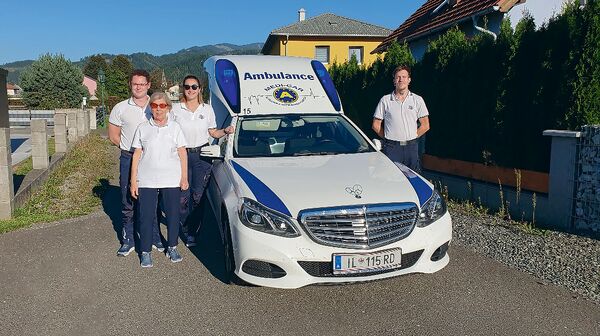 ÖAMTC-Clubmitglieder stehen gemeinsam mit Sanitätern vor einem Krankenfahrzeug.