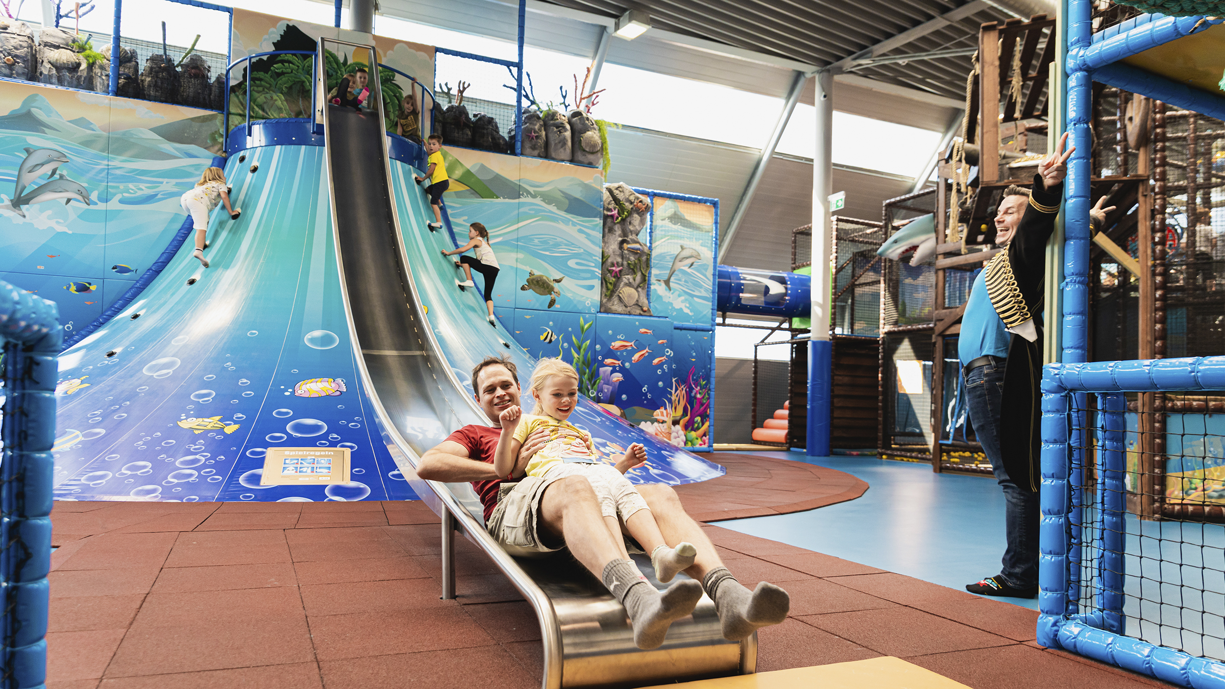 Große Rutsche beim Klettervulkan auf der ein Mann gerade herunterrutscht am Indoor-Spielpatz 