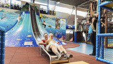 Große Rutsche beim Klettervulkan auf der ein Mann gerade herunterrutscht am Indoor-Spielpatz