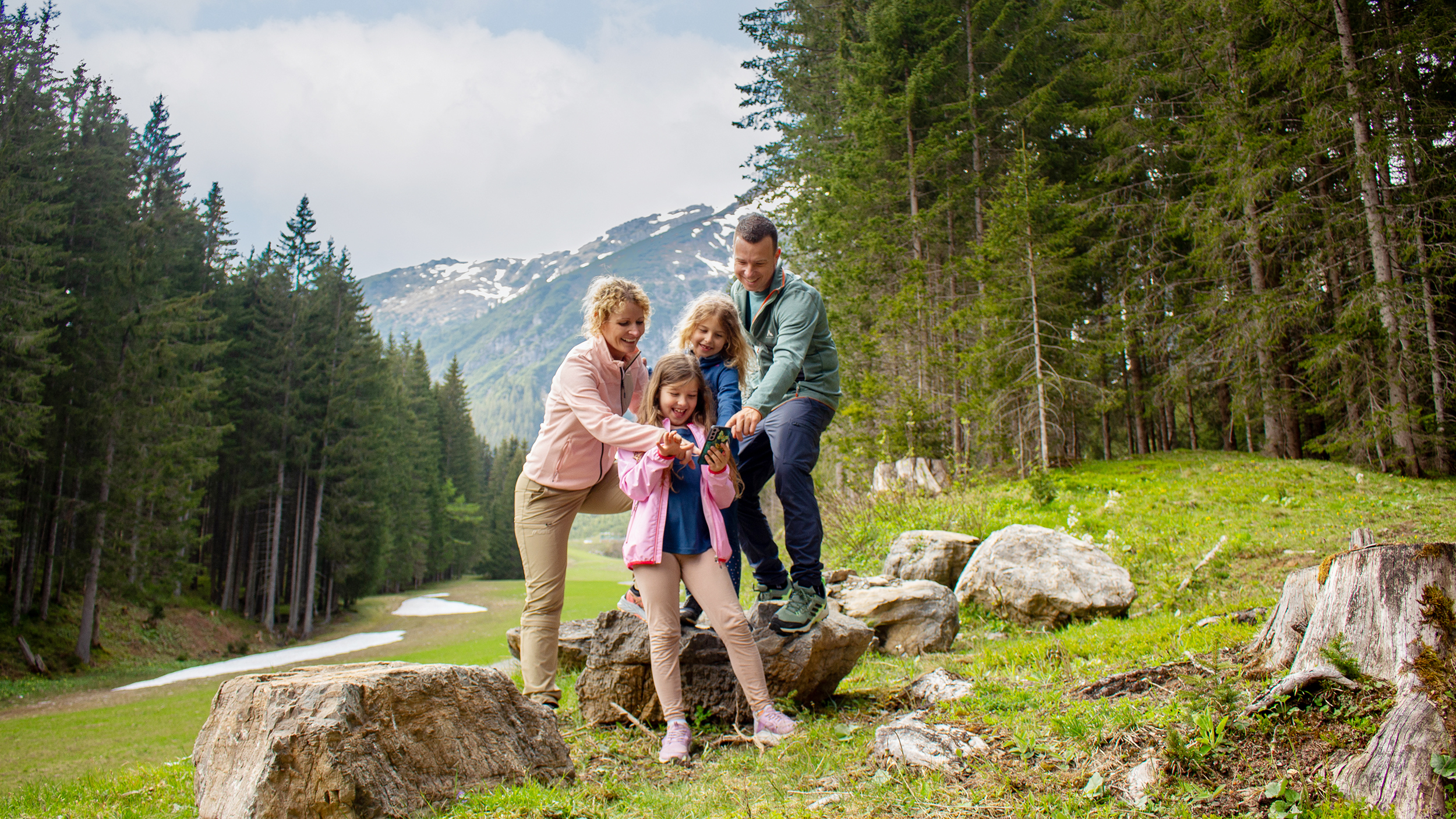 Eine Familie beim Wandern. Sie stehen auf einem felsigen Weg und betrachten das Handy, da es ein digitales Wandererlebnis ist.