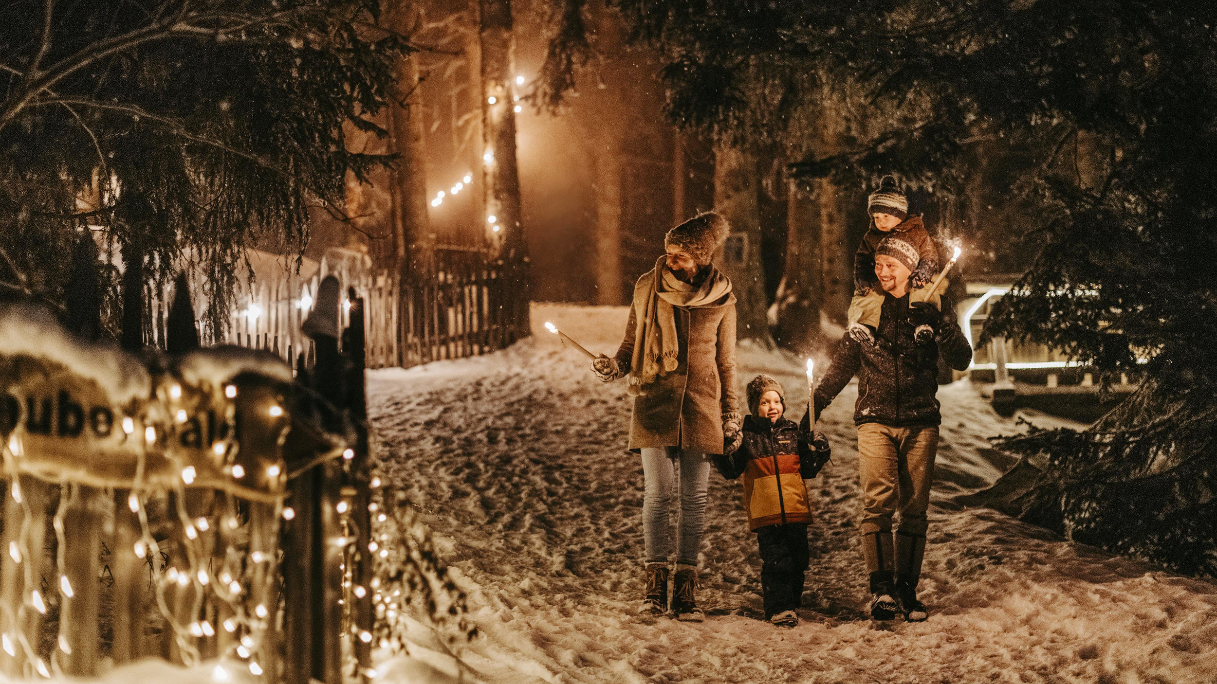 Eltern gehen mit zwei Kindern im Schnee im Wald. Die Werg ist mit beleuchtet.