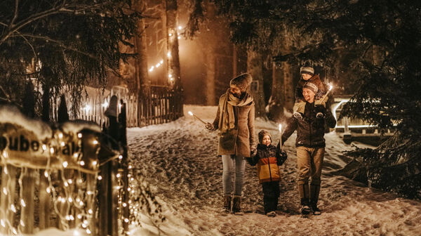 Eltern gehen mit zwei Kindern im Schnee im Wald. Die Werg ist mit beleuchtet.