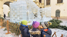 drei Kinder stehen vor der Eiskrippe und zwei Kids geben sich ein Bussi.