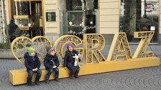 Die Drillinge sitzen in der Stadt auf dem Schriftzug "I love Graz"
