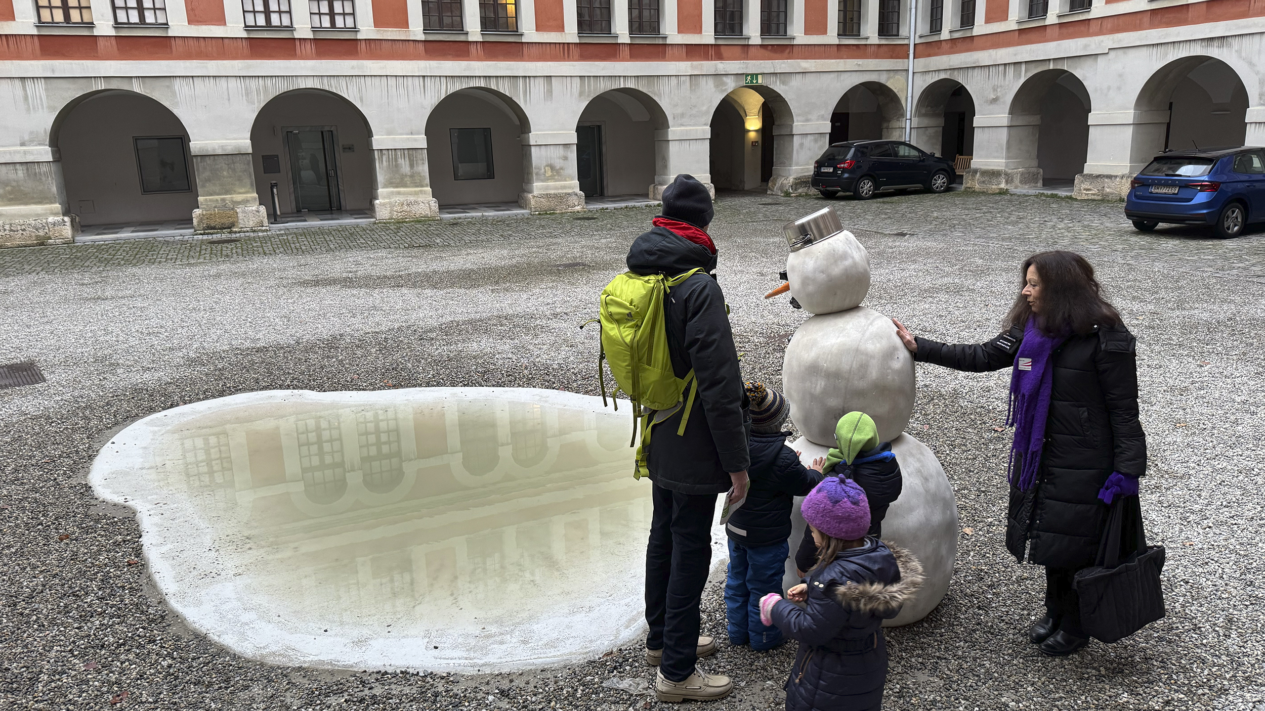 Der Schneemann aus Stein samt Regenlacke wird von den Kindern, dem Papa und der Fremdenführerin betaunt.