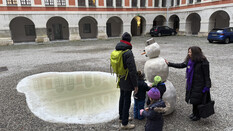 Der Schneemann aus Stein samt Regenlacke wird von den Kindern, dem Papa und der Fremdenführerin betaunt.